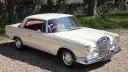 Ivory Mercedes 250 SE Coupe shown from a raised right side angle, with red leather interior visible through the windows.