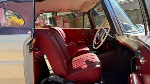 Classic Mercedes 250 SE Coupe interior with rich red leather seats, wood dashboard and vintage steering wheel.