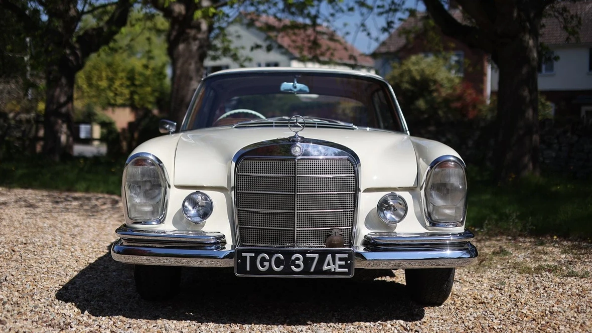 Front view of ivory Mercedes 250 SE Coupe with chrome grille, classic headlights and red leather cabin.