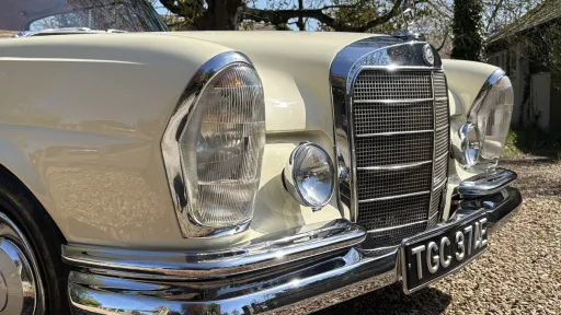 Close-up front detail of ivory Mercedes 250 SE Coupe with chrome grille, headlights and bumper.