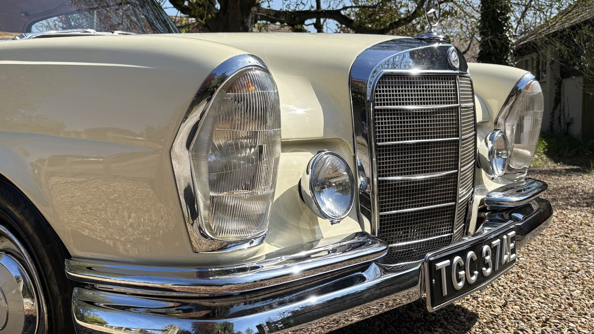 Close-up front detail of ivory Mercedes 250 SE Coupe with chrome grille, headlights and bumper.