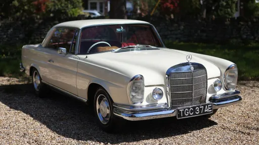 Front right side view of ivory Mercedes 250 SE Coupe wedding car with chrome details and red interior.