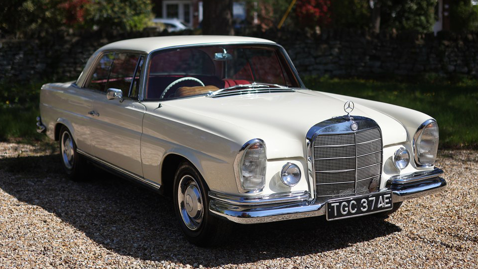 Front right side view of ivory Mercedes 250 SE Coupe wedding car with chrome details and red interior.