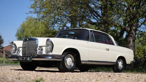 Low front side view of ivory Mercedes 250 SE Coupe parked outdoors with chrome grille and classic styling.