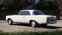 Rear left side view of ivory Mercedes 250 SE Coupe showing its pillarless coupe roofline and chrome bumper.
