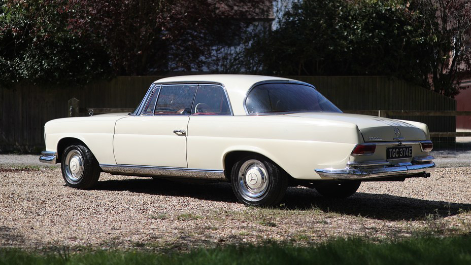 Rear left side view of ivory Mercedes 250 SE Coupe showing its pillarless coupe roofline and chrome bumper.