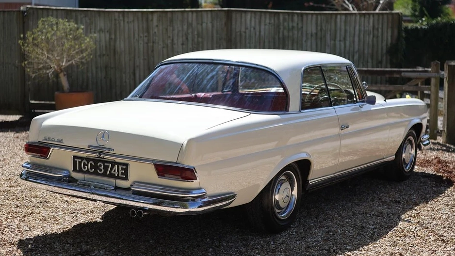 Rear right side view of ivory Mercedes 250 SE Coupe with red leather interior and classic chrome trim.