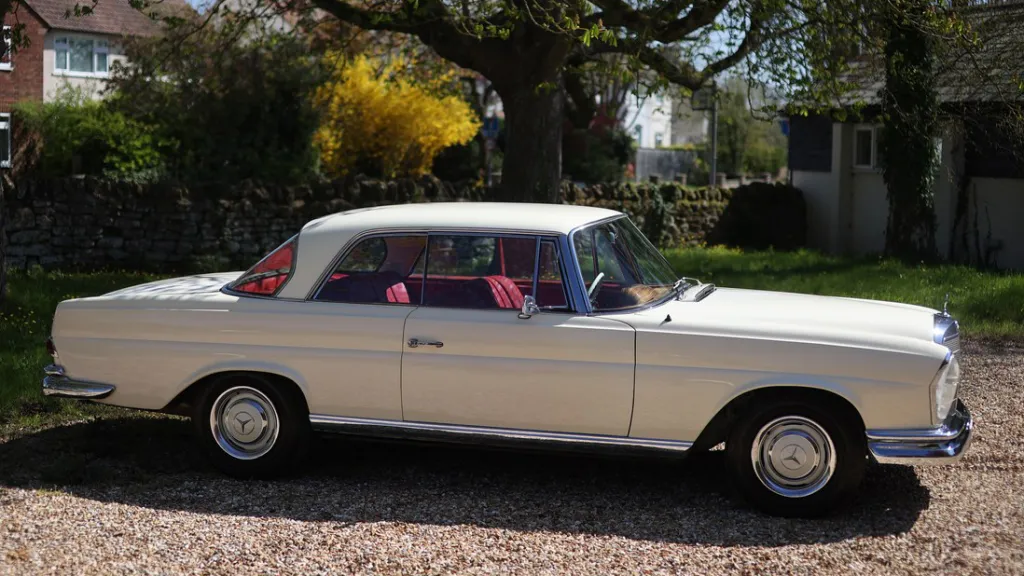 Full right side profile of ivory Mercedes 250 SE Coupe showing long coupe body and red leather cabin.