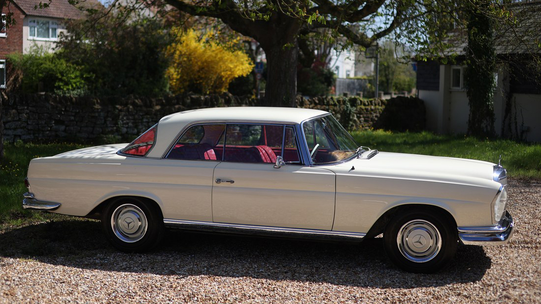 Full right side profile of ivory Mercedes 250 SE Coupe showing long coupe body and red leather cabin.