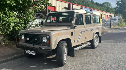 Beige Land Rover Defender wedding car parked outdoors with rugged off road styling and cream roof.
