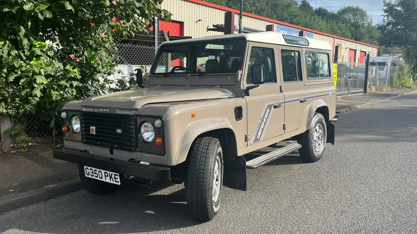 Beige Land Rover Defender wedding car parked outdoors with rugged off road styling and cream roof.