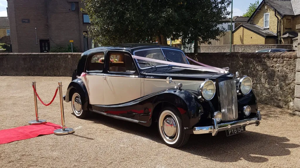 Austin Sheerline wedding car in black and Old English White parked beside red carpet at Kent wedding venue