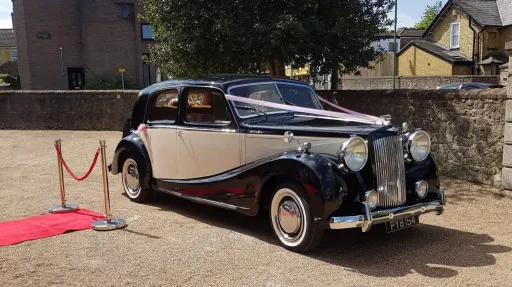 Austin Sheerline wedding car in black and Old English White parked beside red carpet at Kent wedding venue