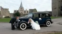 Newlywed couple posing beside classic blue Austin 18 York wedding car outside historic Kent castle venue.