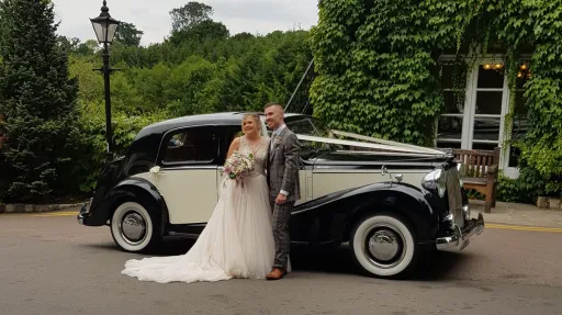 Newlywed couple posing beside Austin Sheerline vintage wedding car at countryside wedding venue in Kent.