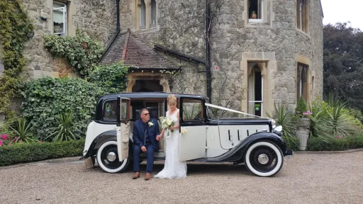 Newlywed couple standing beside 1935 Austin 18 York vintage wedding car outside historic Kent wedding venue.