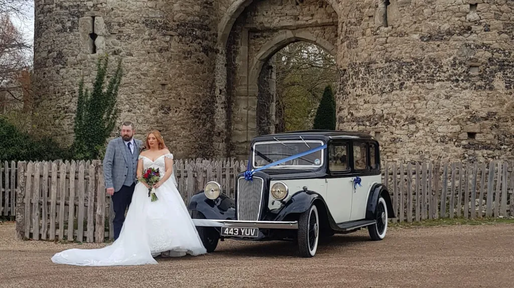 Bride and groom posing beside classic black and ivory Austin 18 York wedding car at Kent countryside venue.