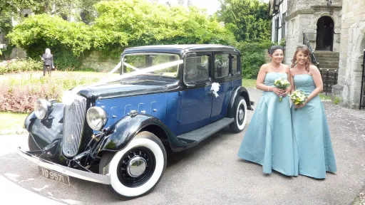 Bridesmaids standing beside blue Austin 18 York vintage wedding car outside church in Kent.