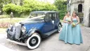 Bridesmaids standing beside blue Austin 18 York vintage wedding car outside church in Kent.