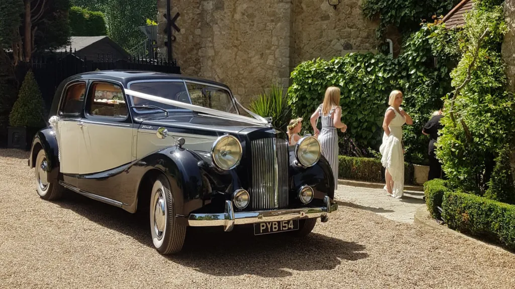 Black and Old English White Austin Sheerline wedding car arriving with bridesmaids at church venue.