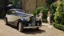 Black and Old English White Austin Sheerline wedding car arriving with bridesmaids at church venue.
