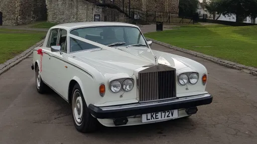 Front three quarter view of a classic Rolls Royce Silver Shadow in Old English White parked outside a stone wedding venue in Kent, featuring chrome grille and timeless luxury styling.