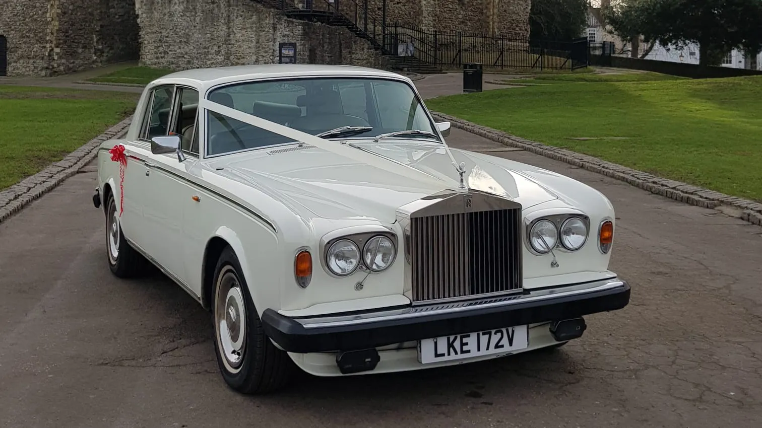 Front three quarter view of a classic Rolls Royce Silver Shadow in Old English White parked outside a stone wedding venue in Kent, featuring chrome grille and timeless luxury styling.