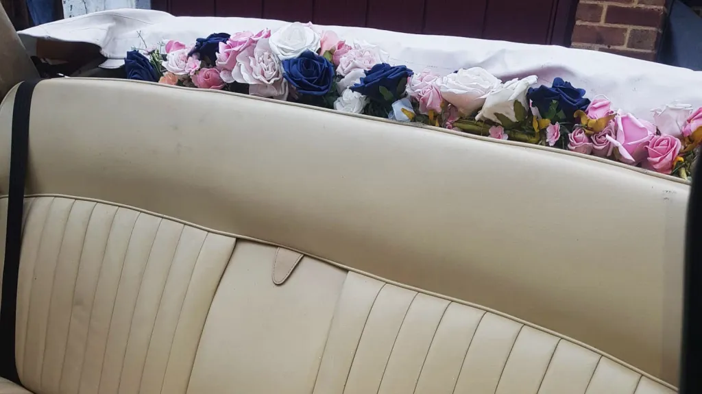 Floral wedding decoration displayed on rear parcel shelf inside classic Daimler limousine.