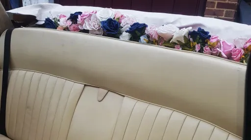 Floral wedding decoration displayed on rear parcel shelf inside classic Daimler limousine.