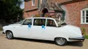 White Daimler limousine landaulette with open rear roof parked outside countryside wedding venue.