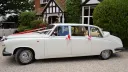 Classic Daimler limousine decorated with wedding ribbons parked outside traditional venue.