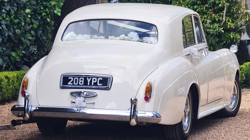 Rear view of a classic Bentley S1 in Old English White showing the elegant rounded vintage bodywork and chrome bumper details outside a wedding venue in Kent.