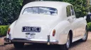 Rear view of a classic Bentley S1 in Old English White showing the elegant rounded vintage bodywork and chrome bumper details outside a wedding venue in Kent.