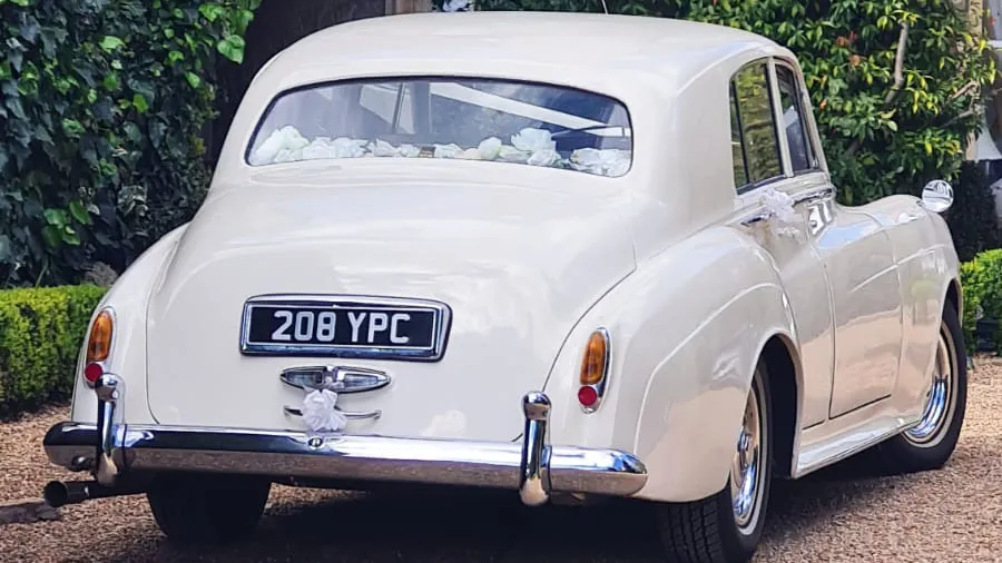 Rear view of a classic Bentley S1 in Old English White showing the elegant rounded vintage bodywork and chrome bumper details outside a wedding venue in Kent.