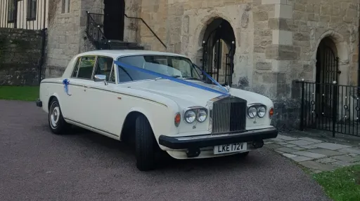 Classic Rolls Royce Silver Shadow wedding car in Old English White decorated with blue wedding ribbons, parked outside a historic church venue in Kent.