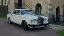 Classic Rolls Royce Silver Shadow wedding car in Old English White decorated with blue wedding ribbons, parked outside a historic church venue in Kent.