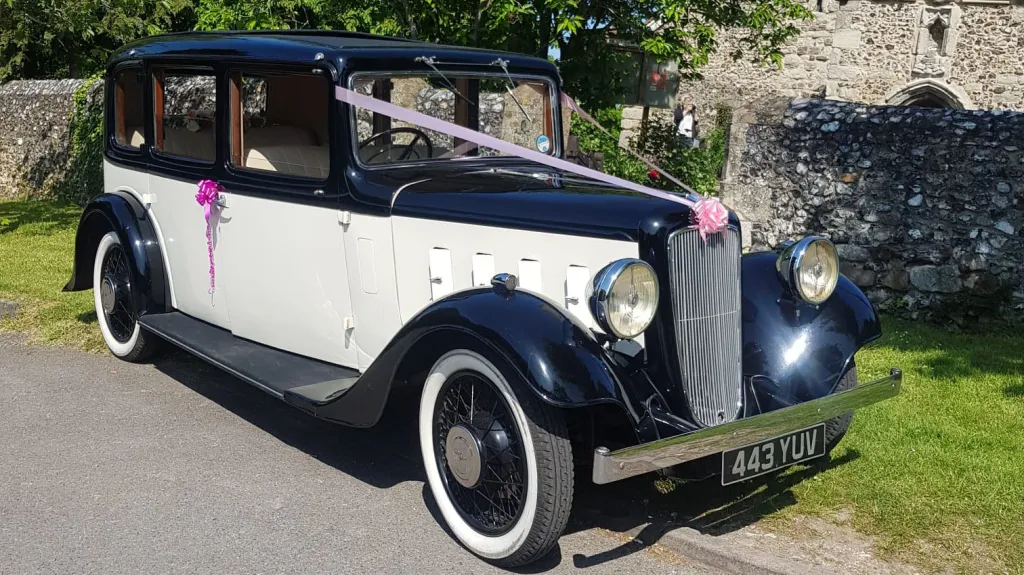 1935 Austin 18 York vintage wedding car decorated with white ribbons and parked outside countryside venue.