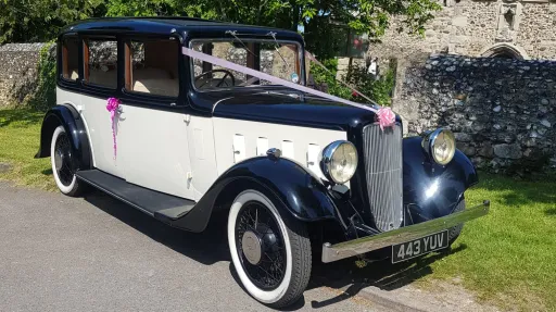 1935 Austin 18 York vintage wedding car decorated with white ribbons and parked outside countryside venue.