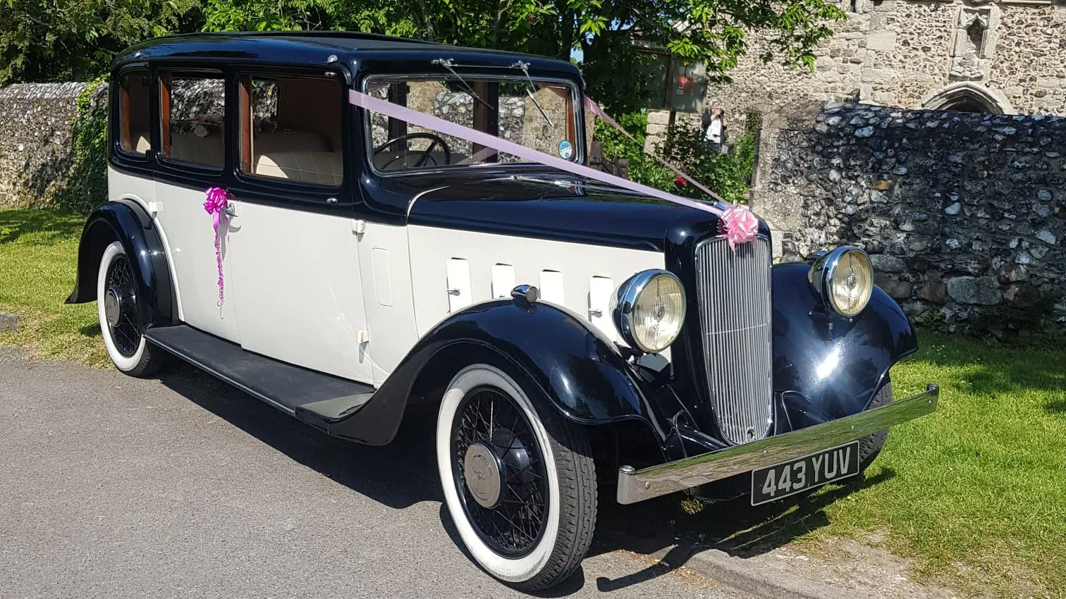 1935 Austin 18 York vintage wedding car decorated with white ribbons and parked outside countryside venue.