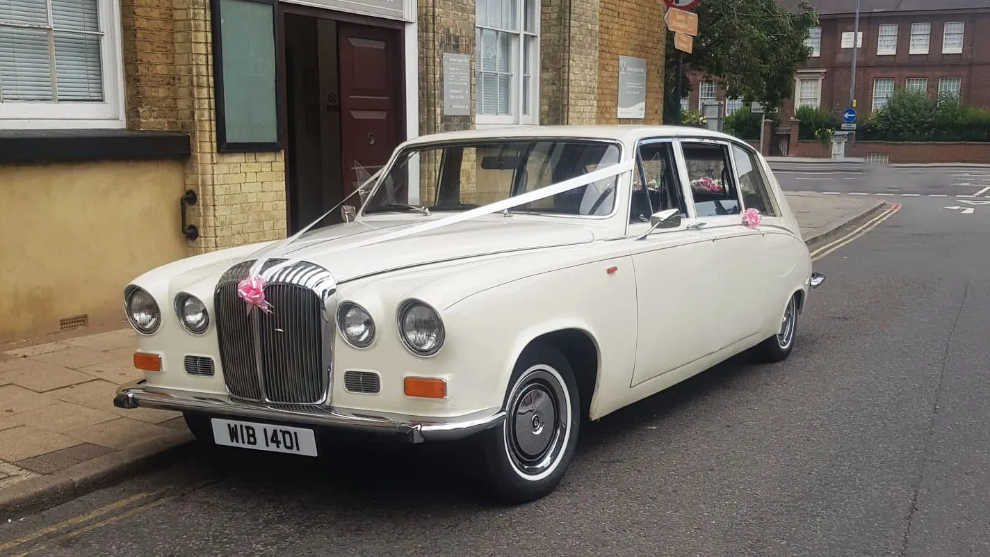 White Daimler DS420 limousine wedding car parked roadside with chrome grille and wedding ribbons.
