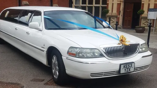 Front side view of white Lincoln Town Car wedding limousine with gold ribbons and chrome detailing.