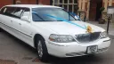 Front side view of white Lincoln Town Car wedding limousine with gold ribbons and chrome detailing.