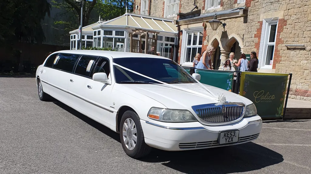 Classic white stretch limousine parked outside wedding venue with long luxury passenger cabin.