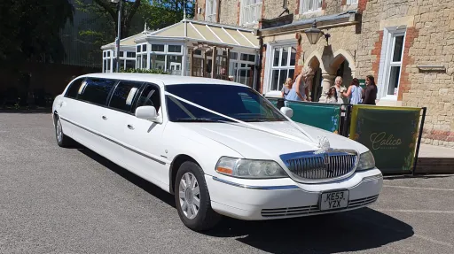 Classic white stretch limousine parked outside wedding venue with long luxury passenger cabin.