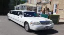 Classic white stretch limousine parked outside wedding venue with long luxury passenger cabin.