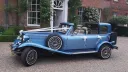 Blue vintage Beauford wedding car with open Sedanca roof outside a wedding venue, decorated with wedding ribbons and chrome detailing.