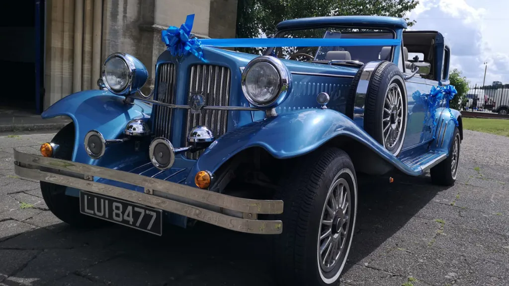 Front view of a blue vintage Beauford wedding car with convertible Sedanca roof, chrome headlights and classic wedding ribbons.