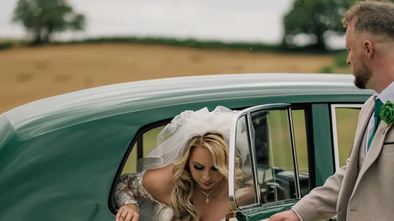 Bride stepping out of a 1957 white Rolls Royce Silver Cloud I with dark green roof and matching dark green leather interior at a countryside wedding in Littlehampton, West Sussex. Classic chauffeur driven wedding car with polished chrome details and elegant vintage styling.