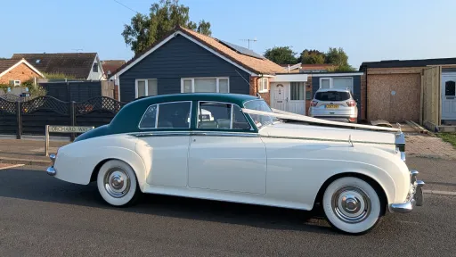 1957 Rolls Royce Silver Cloud I in white with dark green roof parked on a residential street in Littlehampton, West Sussex. Side profile of a classic British luxury wedding car with whitewall tyres and chrome trim.