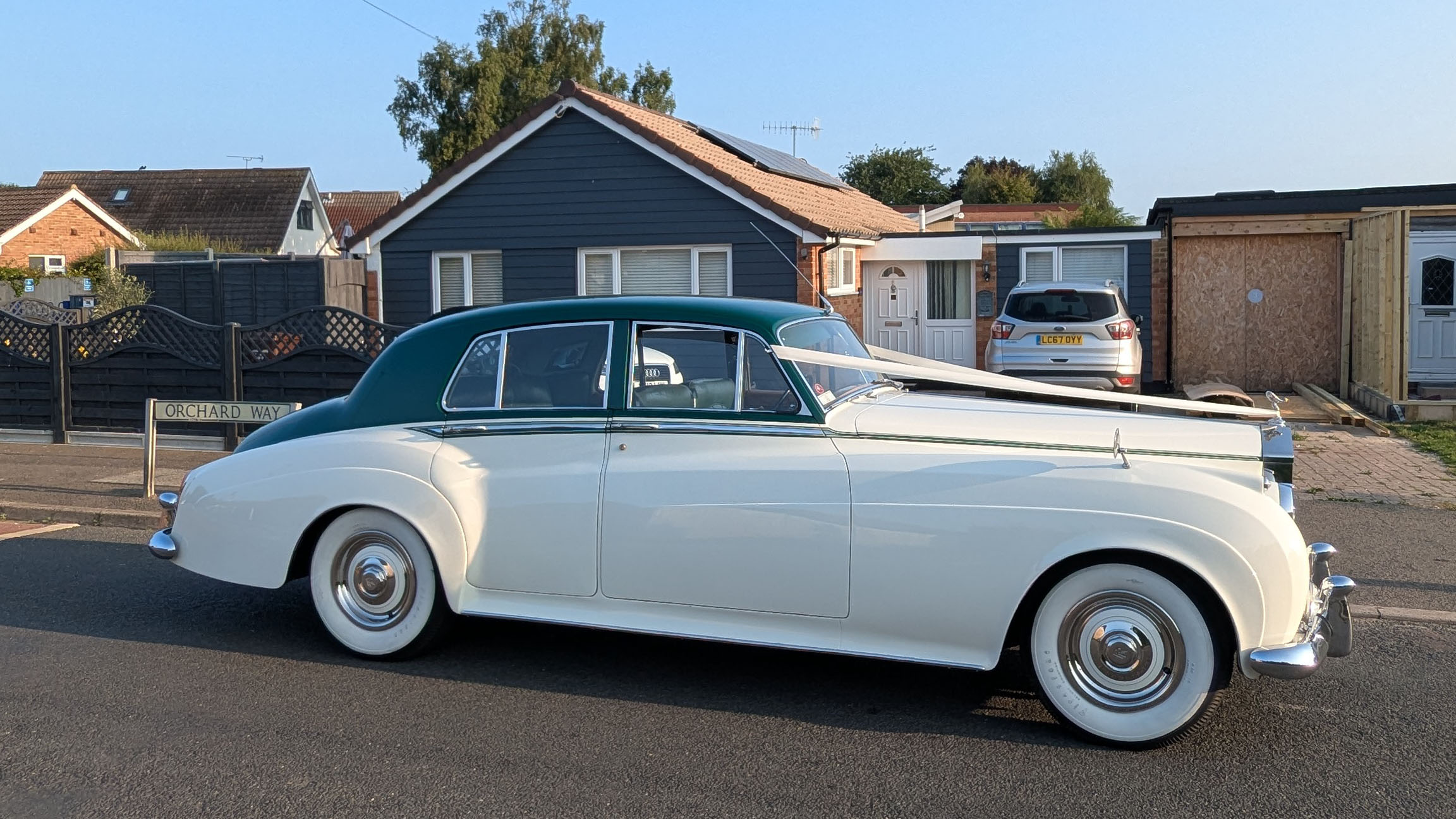 1957 Rolls Royce Silver Cloud I in white with dark green roof parked on a residential street in Littlehampton, West Sussex. Side profile of a classic British luxury wedding car with whitewall tyres and chrome trim.